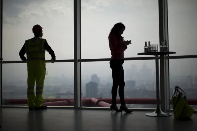 Two apprentices who work on the Queen Elizabeth Olympic Park and were on hand for members of the media to interview, wait by the windows of a viewing gallery in the Orbit sculpture as London's Canary Wharf business district and other parts of the capital stand shrouded in smog in the background during an Olympic Park tour organized for the media, Wednesday, April 2, 2014. (Photo by Matt Dunham/AP Photo)