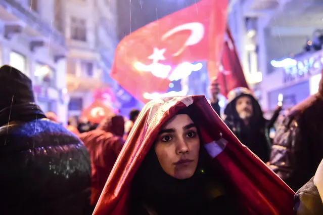 A woman covers herself from rain with the Turkish national flag during a demonstration on March 12, 2017 in front of the Netherlands consulate in Istanbul. The Dutch embassy in Ankara and consulate in Istanbul have been sealed off for “security reasons”, Turkish foreign ministry sources said on Saturday, as tensions soar between Turkey and the Netherlands. (Photo by Yasin Akgul/AFP Photo)