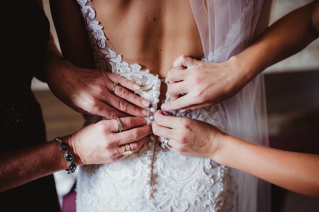 Mother and grandmother's hands buttoning the bride's wedding dress. (Photo by madisonwi/Getty Images)