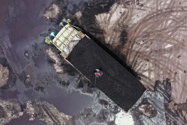 This aerial image shows a worker standing on the back of a truck loaded with coal at the Karya Citra Nusantara (KCN) Marunda port in Jakarta on January 17, 2022, after Indonesia eased an export ban on the commodity. (Photo by Adek Berry/AFP Photo)