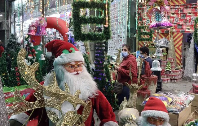 People walk by life-size Santa Claus dolls as they look at boxes with Christmas holiday and New Year decorations for sale at a market in the Shobra district of Cairo, Egypt, 16 December 2021. Although nominally a Christian holiday to celebrate the birth of Jesus Christ, Christmas is also widely celebrated by many non-Christians. (Photo by Khaled Elfiqi/EPA/EFE)
