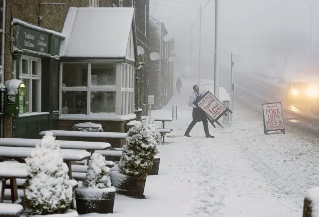 A local butcher carries his shop sign across a snowy pavement in Tow Law, County Durham, Britain, as Storm Eunice makes landfall Friday, February 18, 2022. Millions of Britons are being urged to cancel travel plans and stay indoors Friday amid fears of high winds and flying debris as the second major storm this week prompted a rare “red” weather warning across southern England. (Photo by Owen Humphreys/PA Wire via AP Photo)
