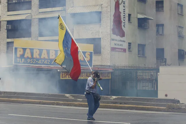 A demonstrator carries a Venezuelan flag amidst tear gas during anti-government protests in Caracas, Venezuela, Wednesday, April 19, 2017. (Photo by Ariana Cubillos/AP Photo)