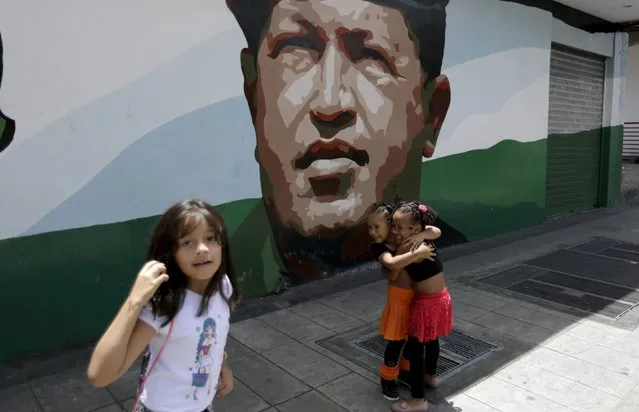 Girls embrace in front of a mural depicting late Venezuelan President Hugo Chavez, at a street in Caracas July 10, 2015. (Photo by Jorge Dan Lopez/Reuters)