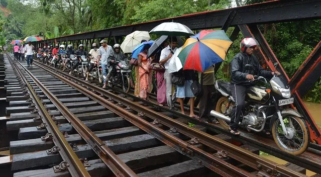 Sri Lankan flood victims cross a narrow access path along a railroad bridge in Puwakpitiya on June 3, 2014 after heavy monsoon rans caused havoc in the western, southern and central regions of the island. Official figures show that at least 18 people were killed and two more were missing after stronger than usual monsoon rains lashed the island. (Photo by Ishara S. Kodikara/AFP Photo)
