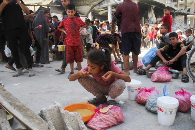 A child eats as Palestinians gather to receive food cooked by a charity kitchen, amid Israel-Hamas conflict, near the ruins of houses destroyed during the Israeli offensive, in Jabalia in the northern Gaza Strip on August 26, 2024. (Photo by Mahmoud Issa/Reuters)