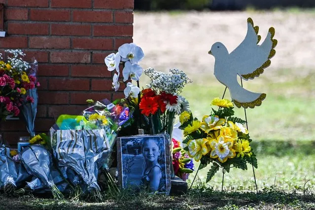 The photo of a little girl, victim of the shooting, is seen by flowers placed on a makeshift memorial in front of Robb Elementary School in Uvalde, Texas, on May 25, 2022. The tight-knit Latino community of Uvalde was wracked with grief Wednesday after a teen in body armor marched into the school and killed 19 children and two teachers, in the latest spasm of deadly gun violence in the US. (Photo by Chandan Khanna/AFP Photo)