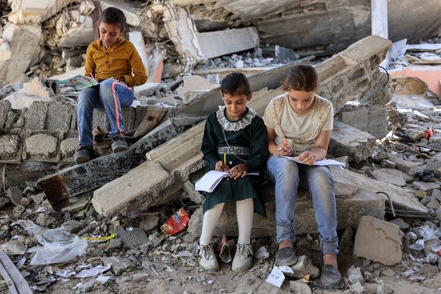 Children write in notebooks by the rubble of destroyed buildings near a tent being used as a make-shift educational centre for primary education students in Jabalia in the northern Gaza Strip on September 8, 2024 amid the ongoing war in the Palestinian territory between Israel and Hamas. (Photo by Omar Al-Qattaa/AFP Photo)