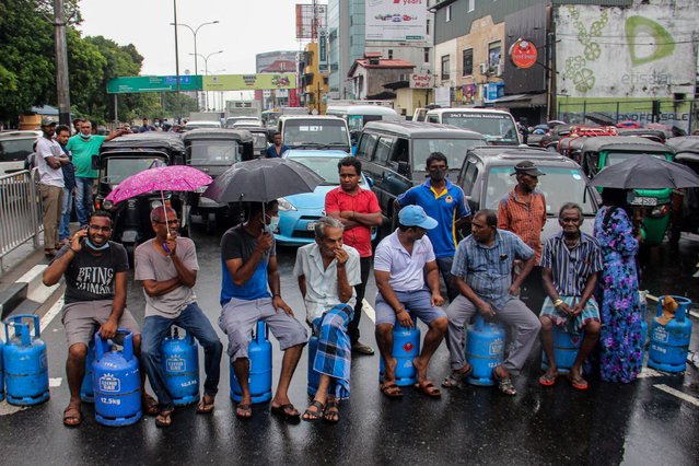 People sit on empty Liquified Gas Cylinders (LPG) as they block a road to protest against shortage of fuel and cooking gas in Colombo on May 13, 2022. Sri Lankans have suffered months of severe shortages of food, fuel and medicine – as well as long power cuts – after the country burnt through foreign currency reserves needed to pay for vital imports. (Photo by AFP Photo/Stringer)