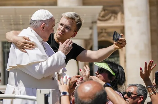 A man hugs Pope Francis to take a selfie photo after he had climbed on the popemobile at the end of the weekly general audience in St. Peter's Square at The Vatican, Wednesday, June 8, 2022. (Photo by Alessandra Tarantino/AP Photo)