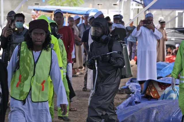 A paramilitary police officer in a hazmat suit walks among pilgrims as he disinfects a tent built on a field where a mass congregation is supposed to be held in Gowa, South Sulawesi, Indonesia, Thursday, March 19, 2020. Indonesia halted the congregation of thousands of Muslim pilgrims and began quarantining and checking their health Thursday to prevent the spread of the new coronavirus. The vast majority of people recover from the new coronavirus. According to the World Health Organization, most people recover in about two to six weeks, depending on the severity of the illness. (Photo by Syaief/AP Photo)