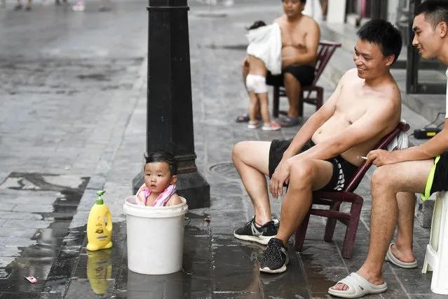A child takes a bath in a bucket to cool off in hot weather on August 15, 2022 in Xiangxi Tujia and Miao Autonomous Prefecture, Hunan Province of China. (Photo by Yang Huafeng/China News Service via Getty Images)