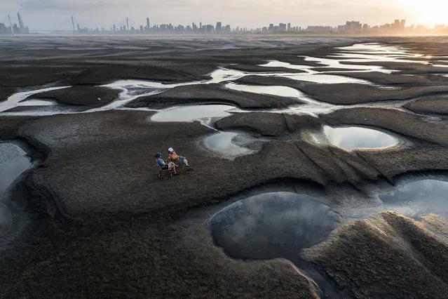 This photo taken on September 2, 2022 shows people sitting on a section of a parched river bed along the Yangtze River in Wuhan in China's central Hubei province. (Photo by AFP Photo/China Stringer Network)