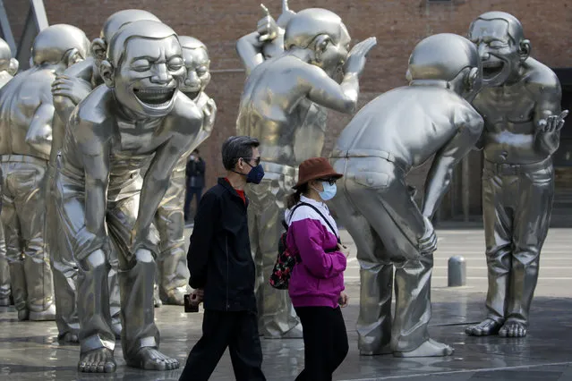 People wearing protective face masks to help curb the spread of the new coronavirus walk by human sculptures on display outside an art gallery in Beijing, Tuesday, April 28, 2020. (Photo by Andy Wong/AP Photo)
