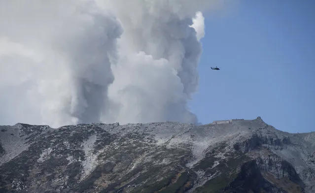A military helicopter, aiding in rescue operations, flies above Mount Ontake as it continues to erupt, Sunday, September 28, 2014, in Nagano prefecture. Military helicopters plucked several people from the Japanese mountainside Sunday after a spectacular volcanic eruption sent officials scrambling to reach many more injured and stranded on the mountain. (Photo by Koji Ueda/AP Photo)
