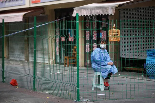 A worker in a protective suit sits behind a barrier at a sealed area following the coronavirus outbreak, in Shanghai, China on October 11, 2022. Keen to avoid a reprise of the economically and psychically scarring lockdown in April-May, Shanghai said late on Monday that all its 16 districts were to conduct mass testing at least twice a week until Nov. 10, a step up from once a week under a regime imposed after the last lockdown. (Photo by Aly Song/Reuters)
