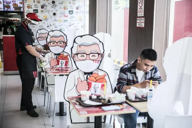 Visitors enjoy food at a table bounded by a banner with a character fast food restaurant Kentucky Fried Chicken, in Jakarta, Indonesia, on June 23, 2020. The display banner is useful for limiting physical distance for visitors who eat on the spot. The Indonesian government has imposed a new set of regulations known as “new normal”, which will be implemented in stages starting in early June for some provinces. (Photo by Jefta Images/Barcroft Media via Getty Images)