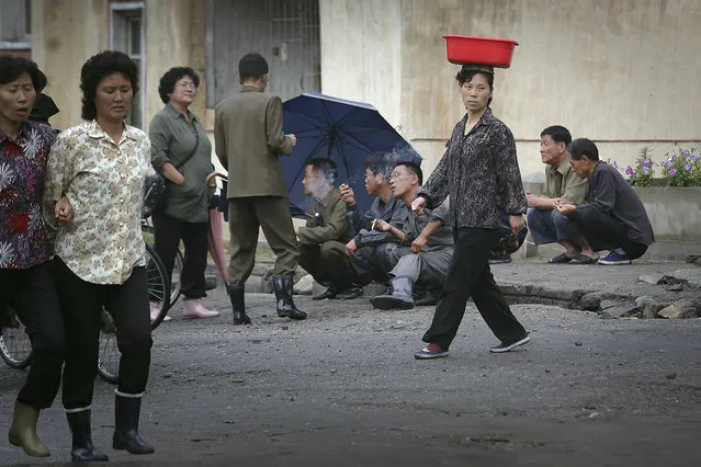 A North Korean woman balances a pail on her head while she walks past men smoking by the road at the end of a work day on Wednesday, June 22, 2016, in Wonsan, North Korea. (Photo by Wong Maye-E/AP Photo)