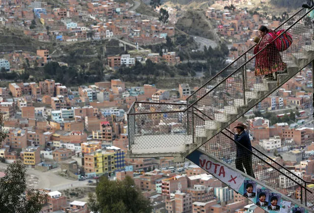 A man an a woman walk through the stairs of an overpass decorated with posters of Bolivia's President Evo Morales in La Paz, Bolivia Thursday October 9, 2014. Bolivia will hold general elections on Sunday. Morales is seeking re-election under the Movement Toward Socialism Party, MAS. (Photo by Enric Marti/AP Photo)