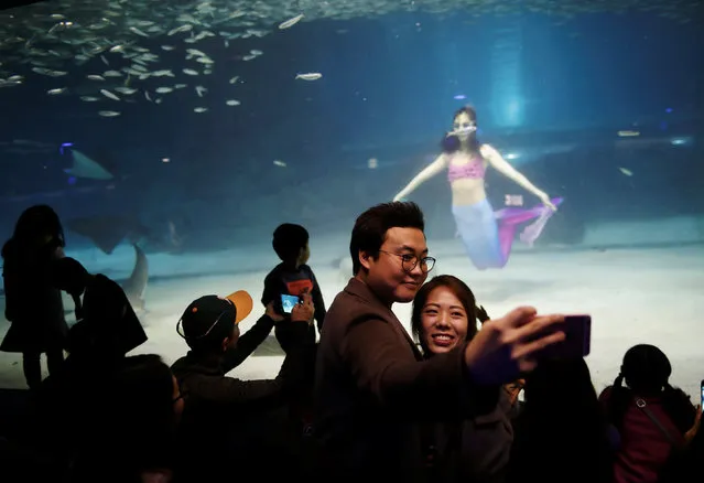 People take a selfie with a diver dressed in a mermaid costume during a promotional event for Christmas “Sardines Feeding Show with Santa Claus” at the Coex Aquarium in Seoul, South Korea, December 10, 2017. (Photo by Kim Hong-Ji/Reuters)