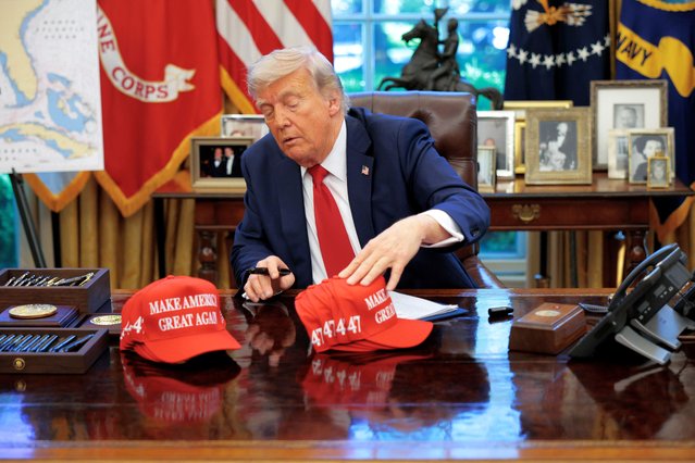 President Donald Trump adjusts “Make America Great Again” hats as he prepares to sign executive orders in the Oval Office at the White House on April 23, 2025 in Washington, DC. The seven executive orders were related to education policy. (Photo by Chip Somodevilla/Getty Images)