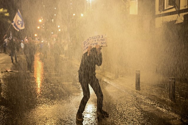 A person covers themselves with a sign as police use water cannons to disperse demonstrators during a protest against Israeli Prime Minister Benjamin Netanyahu's government, amid the ongoing conflict between Israel and the Palestinian Islamist group Hamas from Gaza, in Tel Aviv, Israel, on February 24, 2024. (Photo by Dylan Martinez/Reuters)