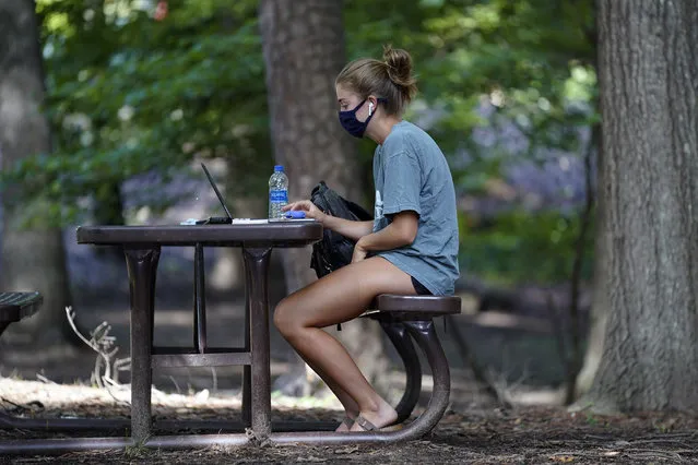 In this August 18, 2020, file photo, a student works outside Ehrighaus dormitory on campus at the University of North Carolina in Chapel Hill, N.C. As more and more schools and businesses around the country get the OK to reopen, some college towns are moving in the opposite direction because of too much partying and too many COVID-19 infections among students. (Photo by Gerry Broome/AP Photo/File)