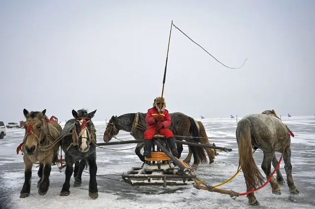A fisherman cracks a whip as horses wheel a device linked to a fishing net during the annual Chagan Lake Winter Fishing Festival in Songyuan, in northeastern China's Jilin province on December 28, 2022. (Photo by Jade Gao/AFP Photo)