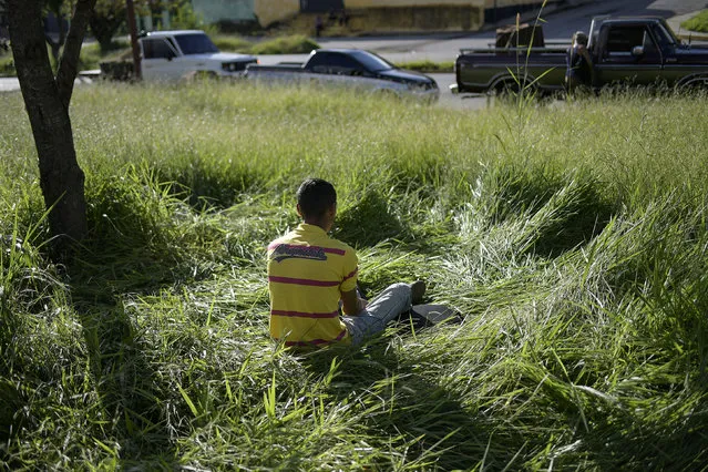 A man wakes up after sleeping on the grass next to his vehicle on his fourth day waiting in line to get a government gasoline coupon to fill up the tank in Merida, Venezuela, Monday, September 21, 2020. Gasoline shortages have returned to Venezuela, that holds the world's largest oil reserves, but it is unable to refine enough crude to meet its domestic needs. (Photo by Matias Delacroix/AP Photo)
