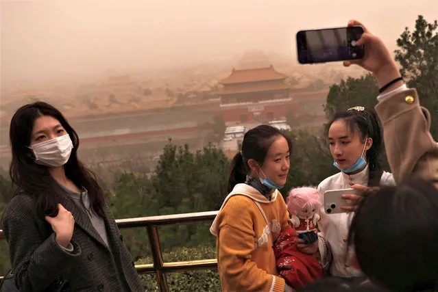 People pose for pictures with the Forbidden City in the background, as the city is shrouded in smog amid a sandstorm, in Beijing, China on March 10, 2023. (Photo by Tingshu Wang/Reuters)