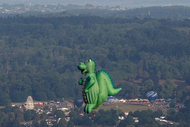 A dinosaur-shaped hot air balloon flies during a mass launch, with the site of the annual Bristol International Balloon Fiesta visible in the background, in Bristol, Britain, on August 8, 2025. (Photo by Toby Melville/Reuters)