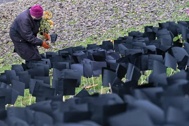 A photo taken on December 9, 2020 at the “Bikas” (Bull) Park in Budapest's 11th district shows an elderly woman placing flowers in front of several thousand black paper flags set up by activists of opposition political party Democratic Coalition, in tribute to the people who died during the novel coronavirus (Covid-19) pandemic, as the number of reported deaths surpassed 6000 in Hungary. (Photo by Attila Kisbenedek/AFP Photo)