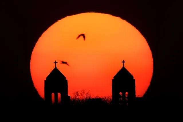 Birds fly past the twin steeples of the Hosanna Karen Baptist church as the sun sets Wednesday, March 29, 2023, in Kansas City, Kan. (Photo by Charlie Riedel/AP Photo)
