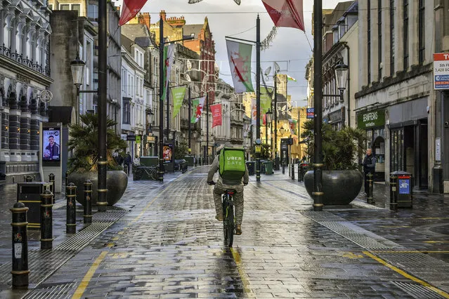 A takeaway delivery cyclist rides down a street in Cardiff city center, Sunday December 20, 2020. In Wales, authorities said they decided to move up a lockdown planned for after Christmas and people must stay at home from 12:01 a.m. Sunday. The move will largely scrap Christmas gatherings in line with the rules for southern England. (Photo by Ben Birchall/PA Wire via AP Photo)