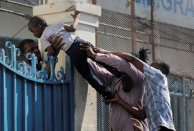 People pass a child over the gates of an immigration office as Haitians gather outside looking to apply for passports, in Port-au-Prince, Haiti on February 15, 2023. (Photo by Ralph Tedy Erol/Reuters)