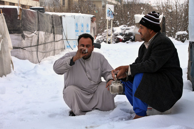 Two Syrian men sit outside their tent as they drink tea, at a refugee camp in al-Majdal village, Bekaa valley, east Lebanon, Thursday, January 8, 2015. Snow fell in the Middle East as a powerful winter storm swept through the region, killing several Syrian refugees in Lebanon and forcing thousands of others who have fled their country civil war to huddle for warmth in refugee camps. (Photo by Hussein Malla/AP Photo)