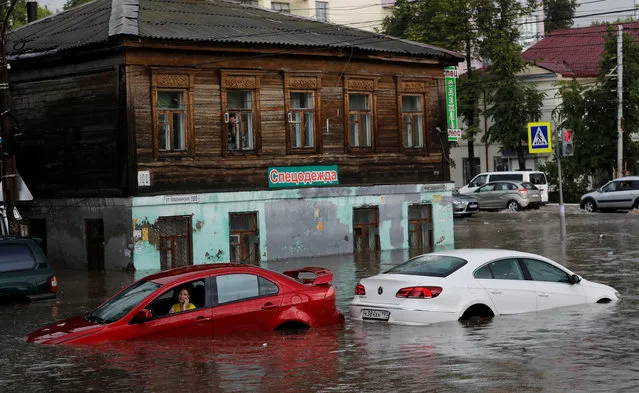 This absolute hero came to the rescue when flash floods in a World Cup city left two women stranded in their submerged cars. Fans in Nizhny Novgorod in western Russia have been basking in sunshine on the banks of the Volga river since the World Cup began. But the lovely weather was put on ice when the heavens opened and a thunderstorm flooded the medieval city. It only took half an hour for the heavy rain to quickly build up rivers of water, bringing traffic to a standstill and stranding motorists. But one man, dressed in a smart shirt and tie, leapt into action to rescue two women from their cars. Pictures show him wading in the waist-high water, dragging them out of their car windows one by one, and carrying them to safety. Due to the presence of a less-than-perfect drainage system, the water quickly rose to dangerous levels. While the flooding briefly dampened spirits at a hilltop fan zone, the sun soon came out again, calm returned, and locals simply shook their heads. “It’s not the first time – we’re used to it”, said one shopkeeper, watching motorists open their bonnets to let their engines dry out. Here: A woman uses her phone as she sits in the car at the flooded street in Nizhny Novgorod, Russia on June 19, 2018. (Photo by Murad Sezer/Reuters)