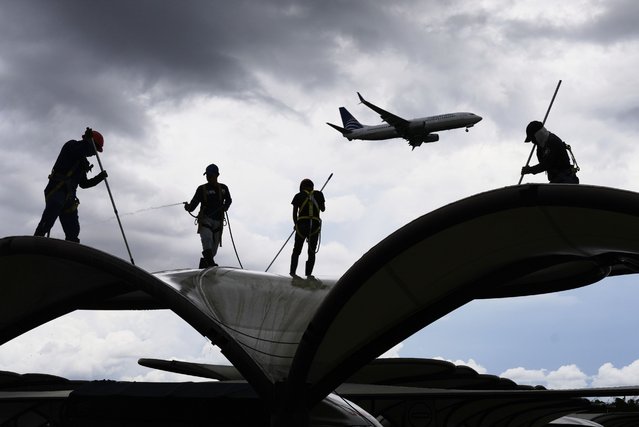 Workers clean a roof at the Tocumen International Airport in Panama City, Thursday, May 22, 2025, as Panama and Venezuela prepare to resume commercial flights nearly a year after suspending them when Panamanian President Jose Raul Mulino refused to recognize the re-election of Venezuelan President Nicolas Maduro. (Photo by Matias Delacroix/AP Photo)