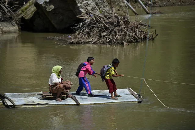 Students pull a rope as they use a bamboo raft to cross a river at a village in Siron, Aceh province on February 17, 2021. (Photo by Chaideer Mahyuddin/AFP Photo)