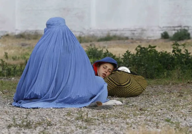 An Afghan refugee woman, clad in a burqa, sits with her sleeping boy as they wait with others to be repatriated to Afghanistan, at the United Nations High Commissioner for Refugees (UNHCR) office on the outskirts of Peshawar, February 2, 2015. (Photo by Fayaz Aziz/Reuters)