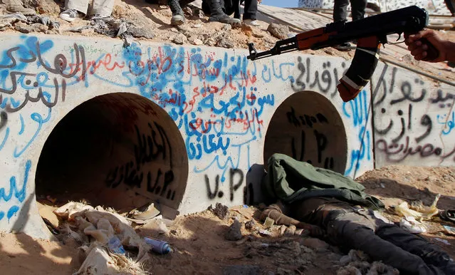 An anti-Gaddafi fighter points at the drain where Muammar Gaddafi was hiding before he was captured in Sirte, Libya October 20, 2011. Gaddafi was killed on Thursday as Libya's new leaders declared they had overrun the last bastion of his long rule, sparking wild celebrations that eight months of war may finally be over. Details of the death near Sirte of the fallen strongman were hazy but it was announced by several officials of the National Transitional Council (NTC) and backed up by a photograph of a bloodied face ringed by familiar, Gaddafi-style curly hair. (Photo by Thaier al-Sudani/Reuters)