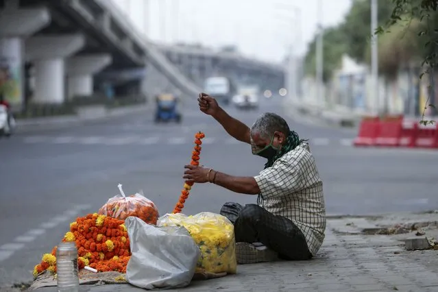 A flower vendor makes garlands by a roadside in Jammu, India, Tuesday, May 4, 2021. COVID-19 infections and deaths are mounting with alarming speed in India with no end in sight to the crisis. (Photo by Channi Anand/AP Photo)
