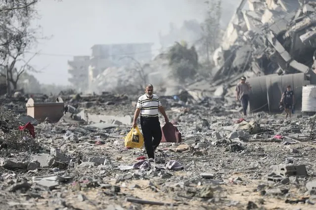 Palestinians walk by buildings destroyed in the Israeli bombardment on al-Zahra, on the outskirts of Gaza City, Friday, October 20, 2023. (Photo by Ali Mahmoud/AP Photo)