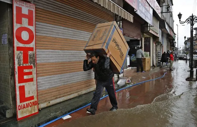 A Kashmiri shopkeeper carries a washing machine on his shoulders to move it to a safer place after heavy rains flooded several areas in Srinagar, Indian controlled Kashmir, Sunday, March 29, 2015. Heavy rains have been reported in several parts of the Kashmir valley. (Photo by Mukhtar Khan/AP Photo)