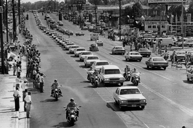 A string of white vehicles follow the hearse carrying the body of rock and roll musician Elvis Presley along Elvis Presley Boulevard on the way to Forest Hills Cemetery in Memphis, Tenn., August 19, 1977. Thousands of people line the route for the city's final tribute to Elvis. (Photo by AP Photo)