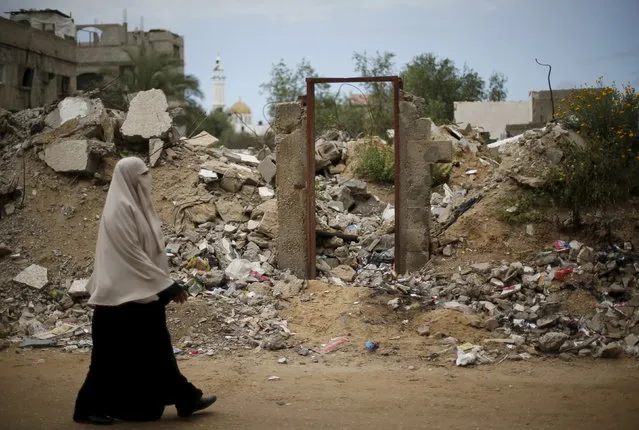 A Palestinian woman walks past the frame of a doorway of a destroyed house, on which British street artist Banksy painted an image of a goddess holding her head in her hand, after the door with the painted image was sold in the northern Gaza Strip, April 1, 2015. (Photo by Mohammed Salem/Reuters)