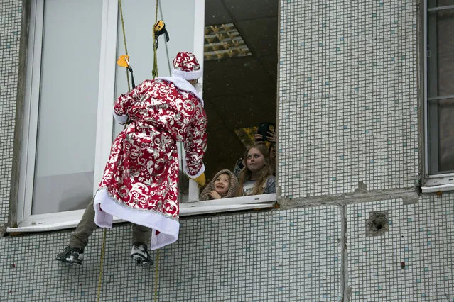 A Russian emergency rescue worker dressed as Ded Moroz (Santa Claus, or Father Frost) greets two girls as he scales the wall of a children hospital in Moscow, Russia, Thursday, December 27, 2018. The action marked the approach of the New Year. (Photo by Alexander Zemlianichenko/AP Photo)