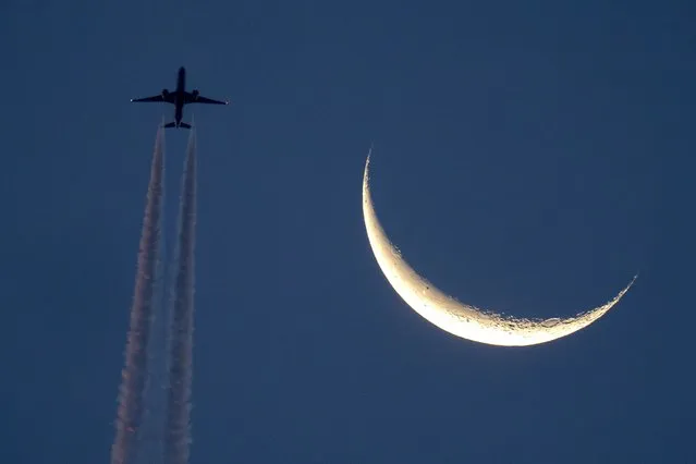 An aircraft passes the decreasing moon over Frankfurt, Germany, Wednesday, October 11, 2023. (Photo by Michael Probst/AP Photo)