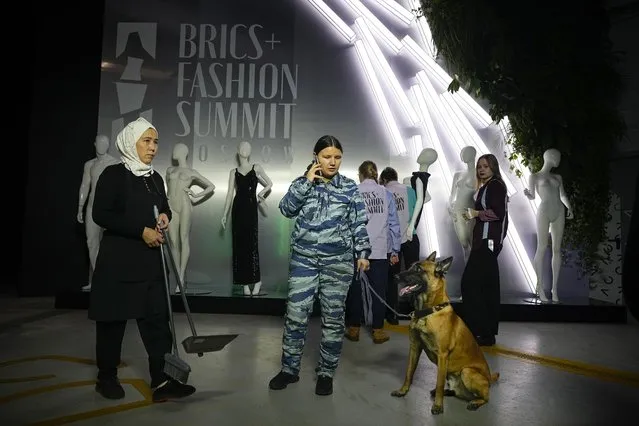 A security officer holds her sniffer dog, as a cleaner walks past prior to the opening of the BRICS+ Fashion Summit in a Parking Gallery at Zaryadye Park near the Kremlin in Moscow, Russia, on Tuesday, November 29, 2023. An international fashion forum in Moscow has brought together designers from Brazil, China, India, South Africa and other countries, an event that underlined Russia's shift away from the West amid the fighting in Ukraine. (Photo by Alexander Zemlianichenko/AP Photo)