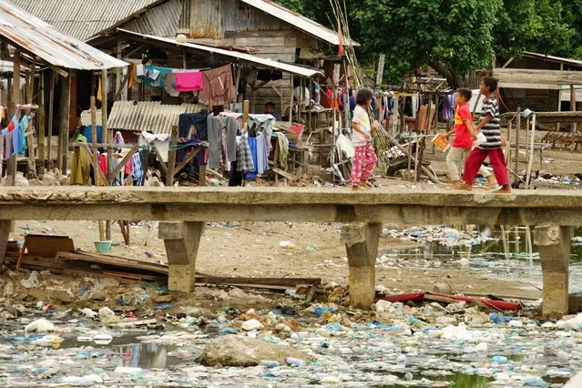 Residents cross a bridge at a river mouth filled with garbages in Lhokseumawe, Aceh on August 22, 2021. (Photo by Azwar Ipank/AFP Photo)